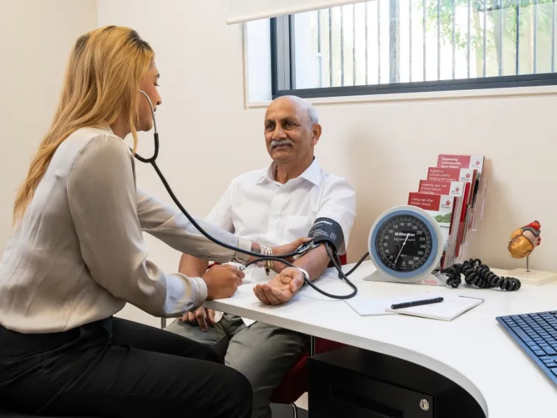 Nurse checking older man’s blood pressure during heart health check, demonstrating importance of monitoring hypertension for preventing heart disease.