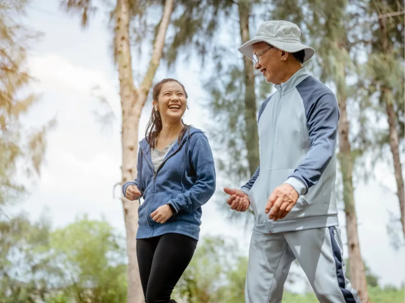 Middle‑aged man and younger woman walking outdoors in park, enjoying heart‑healthy exercise and active lifestyle for cardiovascular health.
