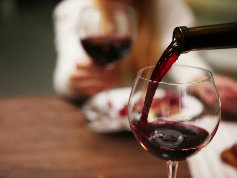 Red wine being poured into a glass at dinner, highlighting alcohol and heart health myth about red wine being good for your heart.