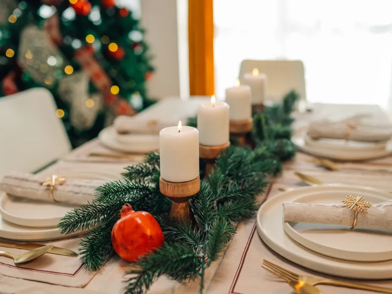 Festive Christmas dining table with candles, evergreen garland and pomegranate centrepiece, elegant holiday place settings ready for a heart-healthy celebration.