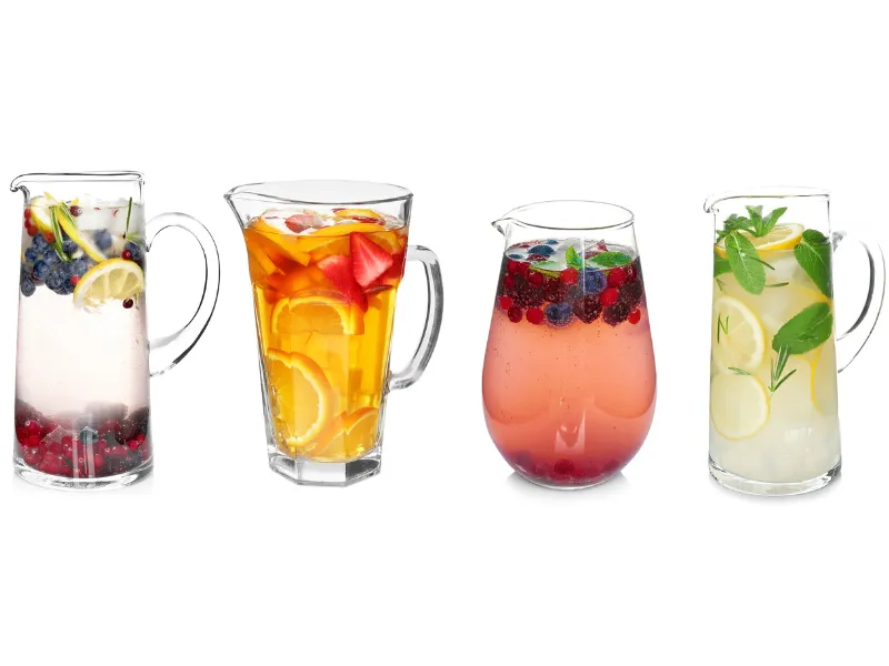 Four glass jugs of colourful fruit infused water with lemon, berries, herbs and citrus slices on white background, healthy low sugar summer drinks