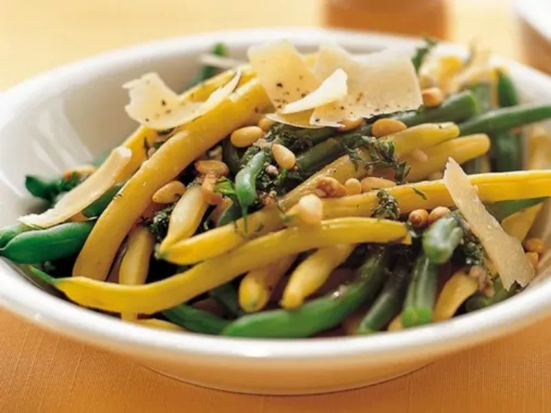 Warm green and yellow bean salad with pine nuts and shaved parmesan in white bowl, healthy vegetable side dish for heart friendly meals.
