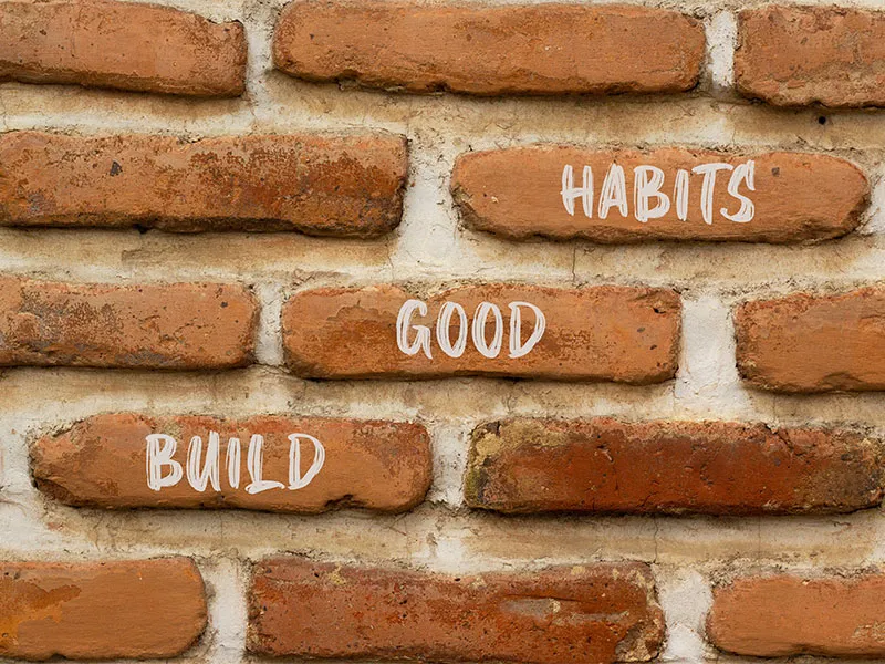 A red brick wall with the words 'build good habits' written on it in white  paint.