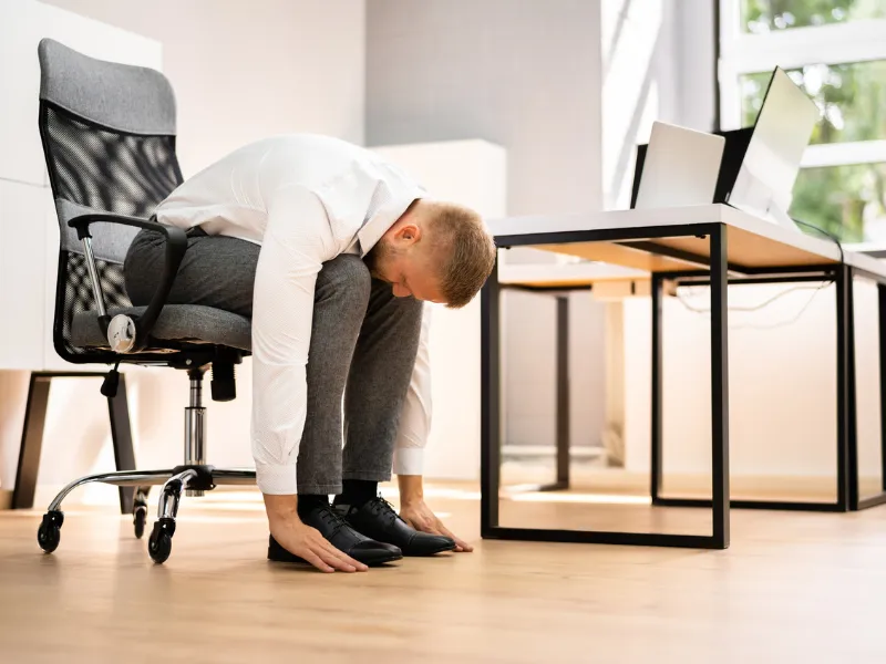 Office worker performing seated forward bend stretch at desk to reduce sitting time.