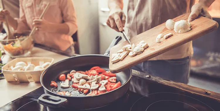 People in a kitchen cooking mushrooms in a frying pan