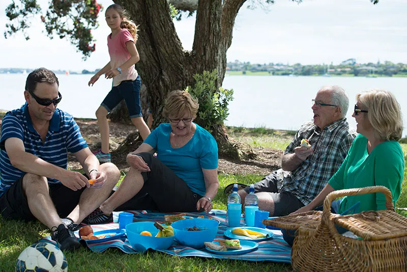 An intergenerational family enjoying a picnic together at a park in New Zealand