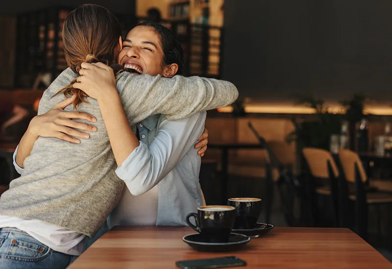 Two women are meeting at a local coffee shop. Friends hugging each other at a cafe. 
