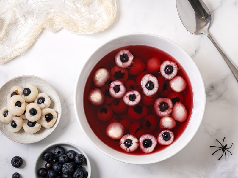 Halloween bowl of lychee and blueberry eyeballs in red syrup for a creepy party dessert.