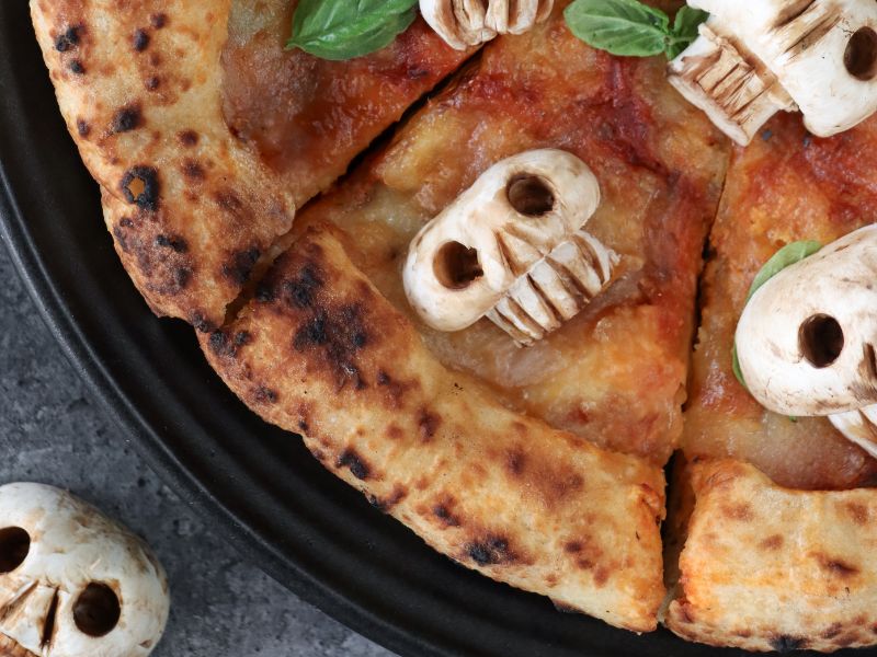 Halloween margherita pizza decorated with mushroom skulls and fresh basil for spooky party food.
