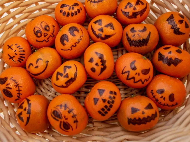 Mandarins decorated with jack-o-lantern faces for healthy Halloween treats in a woven basket