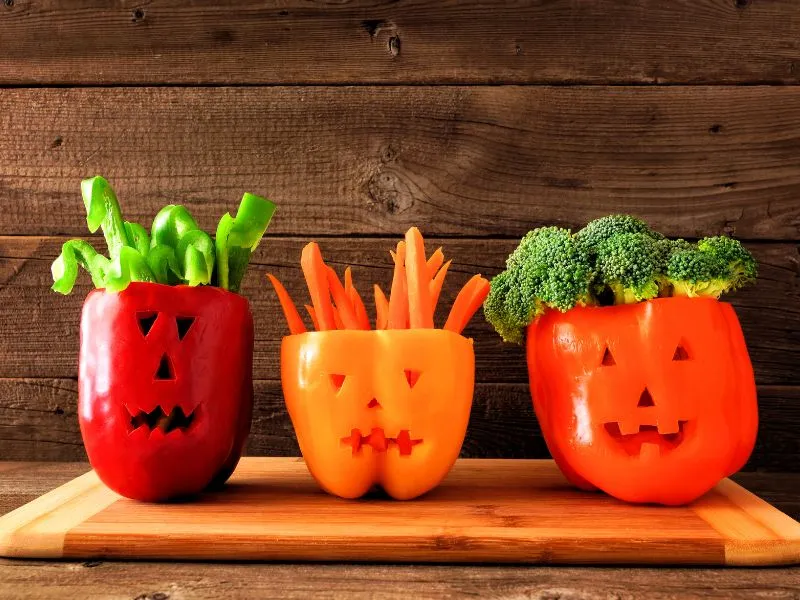 Bell peppers carved as Halloween jack-o-lanterns and filled with fresh vegetables for healthy spooky snacks.