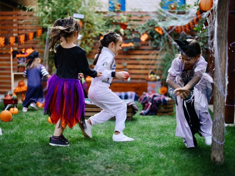 Children playing outside in Halloween costumes during a festive backyard party with decorations.