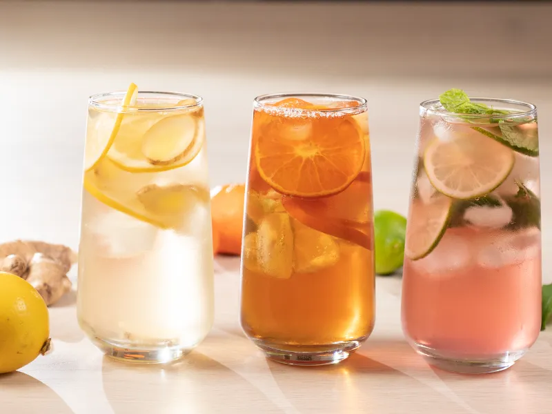 Three tall glasses of homemade iced drinks with lemon, citrus slices, lime and mint, refreshing low sugar summer beverages for healthy hydration.