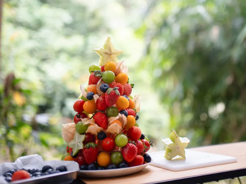 Colourful fresh fruit Christmas tree made from strawberries, grapes, blueberries and cherries on a plate, healthy festive dessert idea outdoors