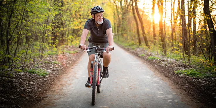 A senior aged man is riding a bike along a track surrounded by trees.