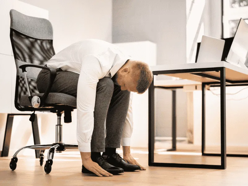 Office worker performing seated forward bend stretch at desk to reduce sitting time.