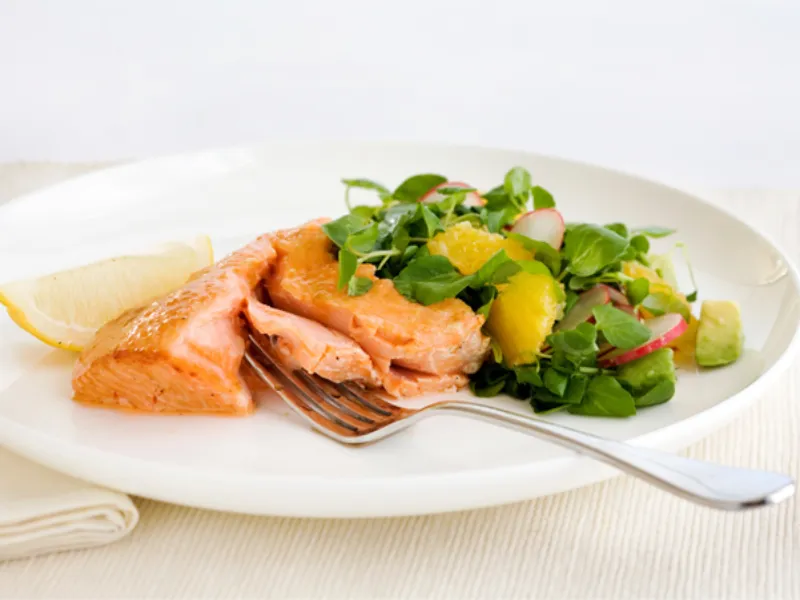 Baked salmon fillet served with fresh green salad of leafy greens, orange segments, radish and avocado on white plate, heart healthy omega-3 rich dinner.