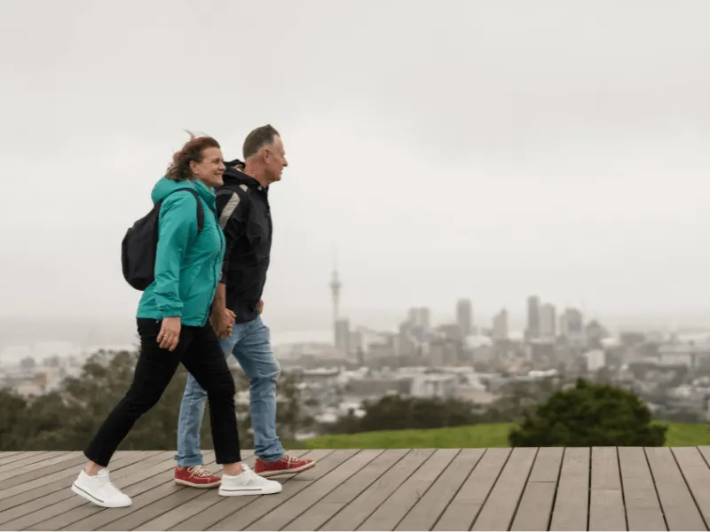 Man and woman walking outdoors on a wooden deck overlooking a city skyline on a cloudy day, emphasizing heart health benefits of regular walking.