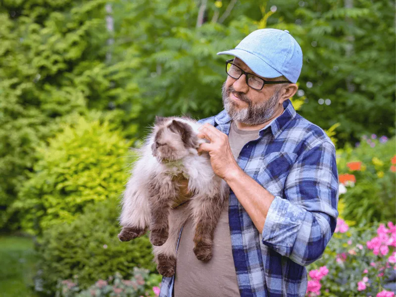 Man holding a fluffy cat in a garden, showing the calming and heart health benefits of spending time with pets.