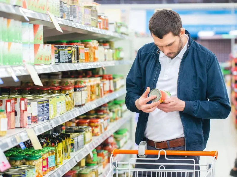 A man in the supermarket reading product label along with a shopping cart