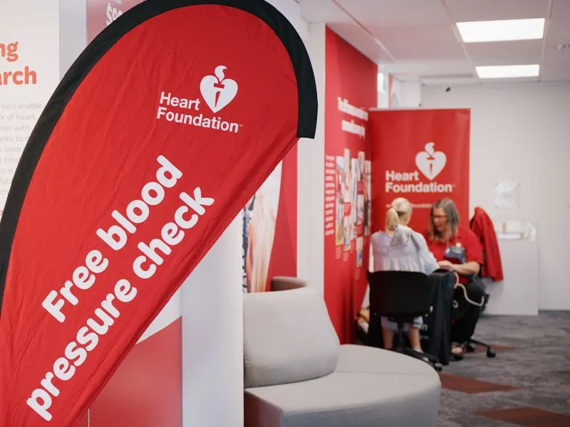 Heart Foundation free blood pressure check event in at Heart Foundation, red Heart Foundation banner promoting free blood pressure checks, people receiving blood pressure screening at Heart Foundation pop up