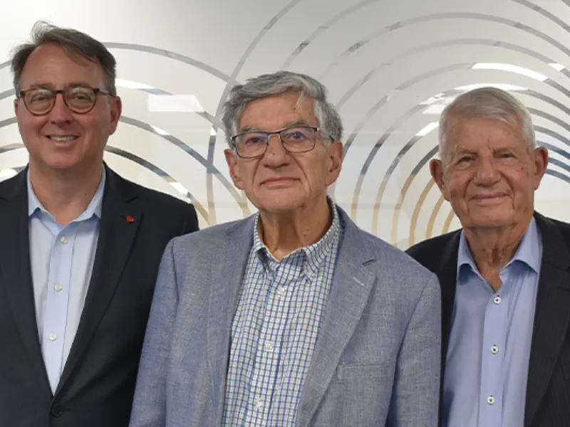 Sir Jim Mann, Clive Nelson and Mike Tomlinson standing and smiling in front of a Heart Foundation heart-pattern backdrop at a New Zealand heart health event.