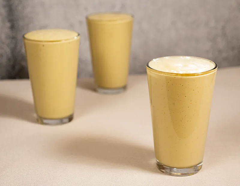 3 glasses of freshly-made avocado and peach smoothie photographed against a neutral background. The smoothie is a golden yellow colour and looks thick and creamy.