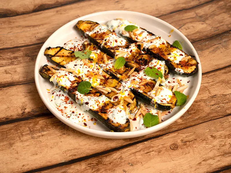 Barbecued courgettes on a white plate, drizzled with a mint and yoghurt dressing.