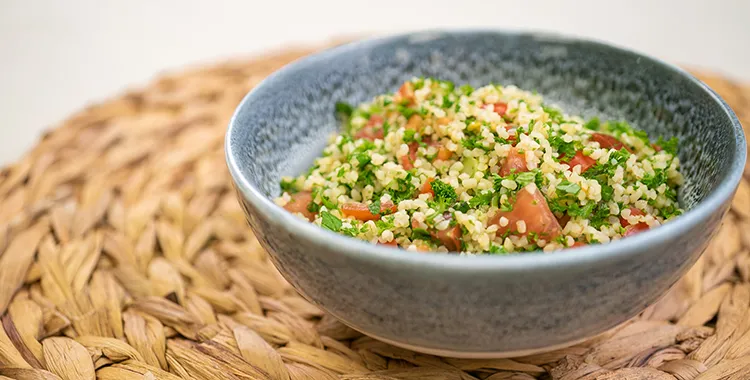 Bulgur wheat tabbouleh—parsley‑forward salad with finely diced tomatoes, mint, scallions, lemon, and olive oil—served in a blue bowl.