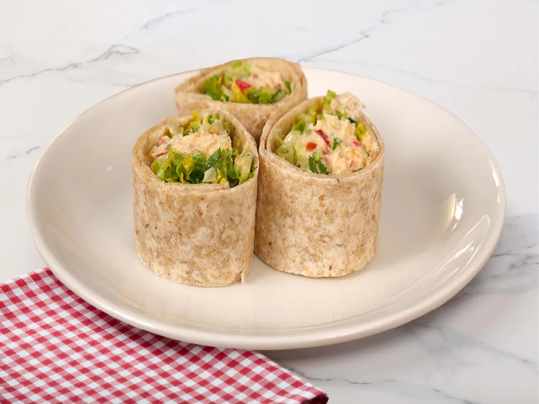 The image shows 3 cylindrical wraps made of wholemeal tortillas. Inside you can see lettuce and the smashed chickpea concoction. The wraps are set on a white plate next to a red and white checked napkin.