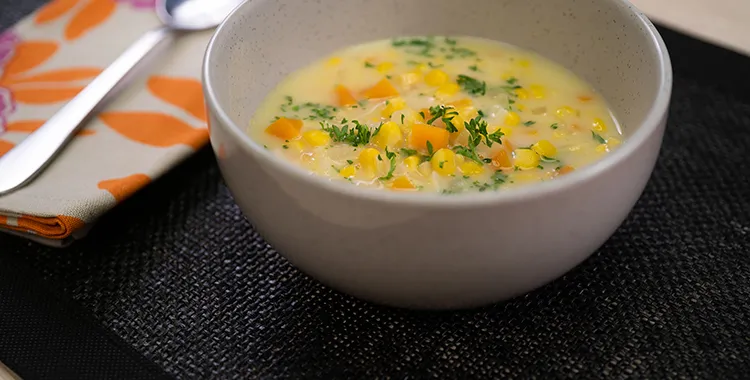 Creamy dairy‑free corn chowder with sweetcorn, potato, and carrot in a coconut‑milk broth, garnished with parsley in a speckled bowl.