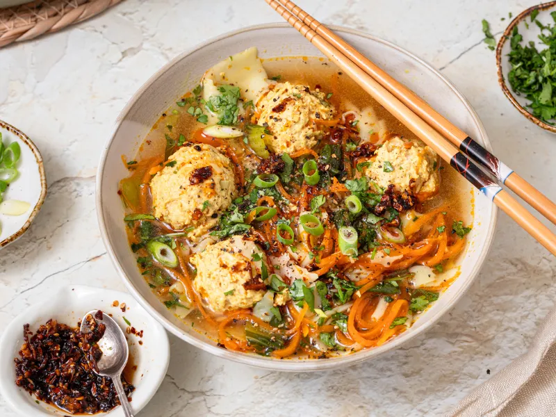 Deconstructed wonton soup with chicken meatballs, carrot noodles, and cilantro in a ceramic bowl with chopsticks.