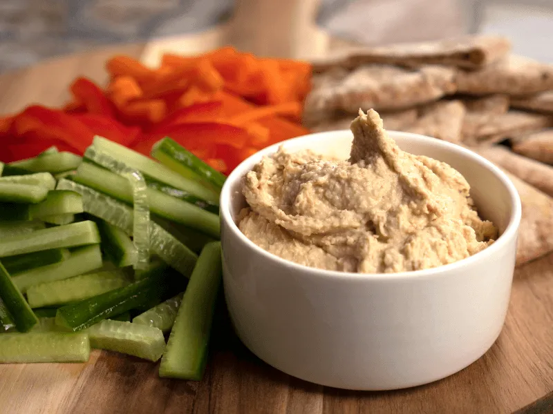 Classic hummus—creamy dip made from chickpeas, tahini, lemon juice, olive oil, and garlic—served with cucumber, carrot sticks, and pita bread.