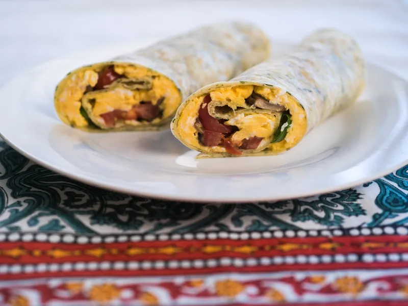 Egg and vegetable burrito cut in half and served on a white plate