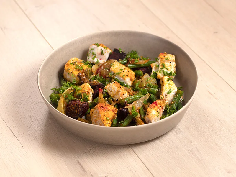 An off-white bowl on a light brown surface holds a serving of fish and beetroot tray bake with green beans
