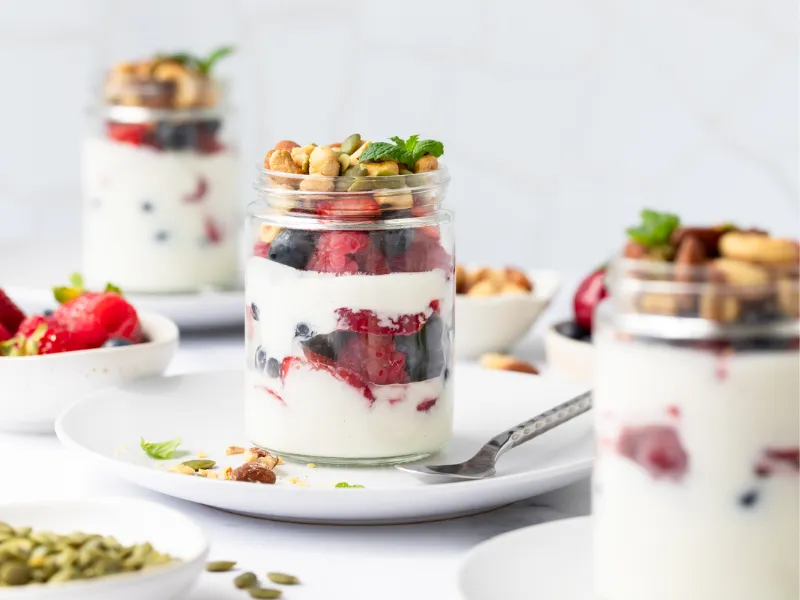Healthy yogurt parfait in a glass jar with layers of Greek yogurt, fresh berries, granola, and nuts, served on a white plate—perfect breakfast or snack idea.
