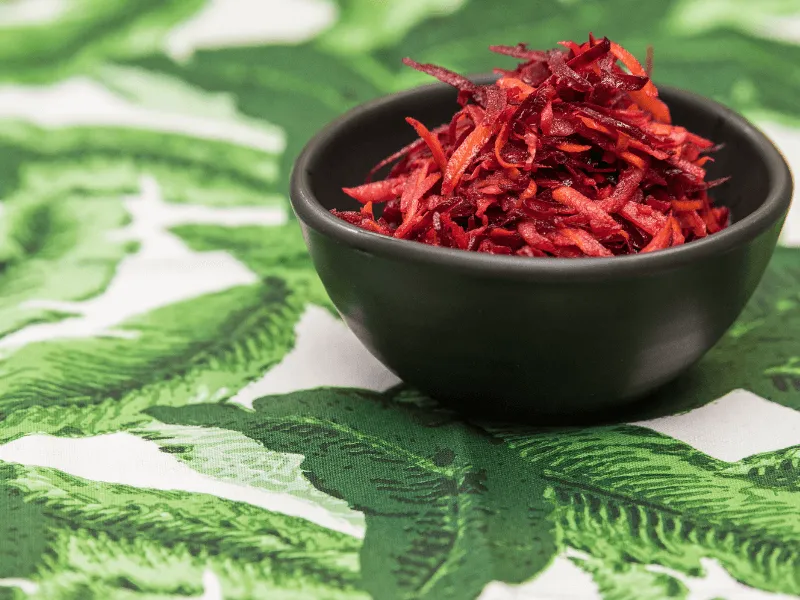 Grated beetroot, carrot, and apple salad in a black bowl, showcasing a vibrant raw slaw of shredded red and orange vegetables.