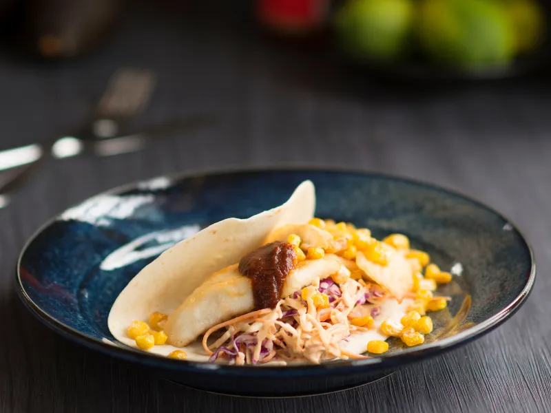 Grilled Baja fish taco with corn, slaw and sauce on a blue plate.
