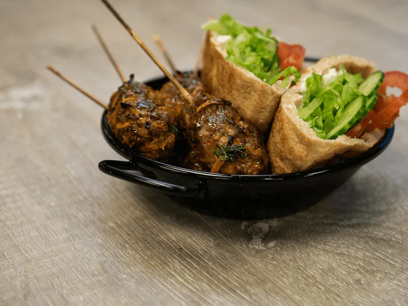 Classic beef burger with a lettuce‑topped patty, sliced tomato and cucumber, shredded cheese, and ketchup in a wholemeal bun on a white plate.