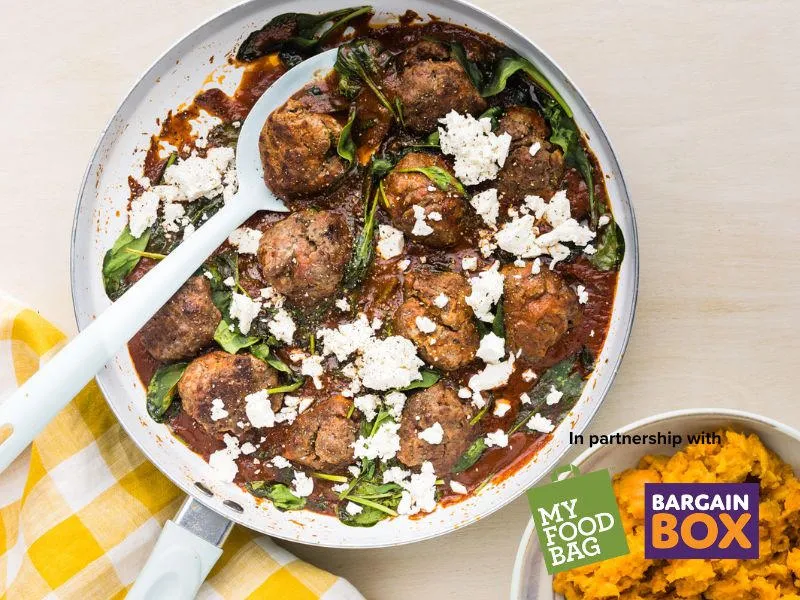 Italian-style meatballs in tomato sauce with spinach and crumbled feta in a white pan, My Food Bag and Bargain Box healthy dinner recipe image