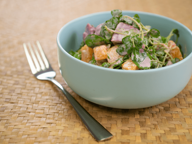 Kūmara and watercress salad with diced cooked sweet potato, fresh watercress, and a creamy mayo‑yogurt dressing, served in a light blue bowl.