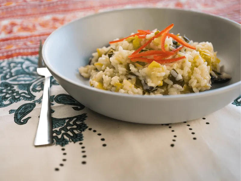 Creamy leek and lemon risotto made with Arborio rice, garnished with thin red capsicum strips, served in a shallow gray bowl.