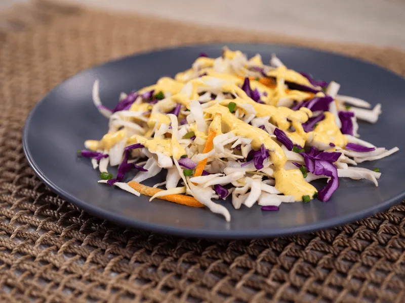 Shredded cabbage slaw with carrots and purple cabbage drizzled with a light mayonnaise dressing on a gray plate.
