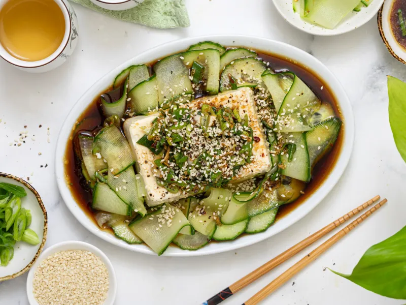 Silken tofu with chilli soy dressing and cucumber ribbons on a white platter, topped with spring onions and sesame seeds, Japanese cold tofu hiyayakko side dish.