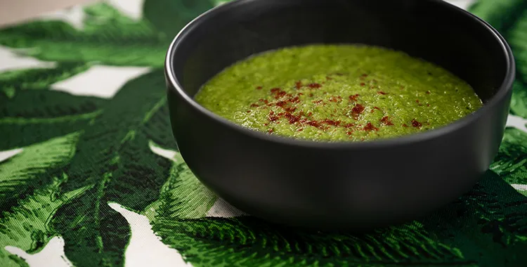 Smooth minted pea soup garnished with a sprinkle of paprika in a black bowl, made with peas, fresh mint, and blended until silky.