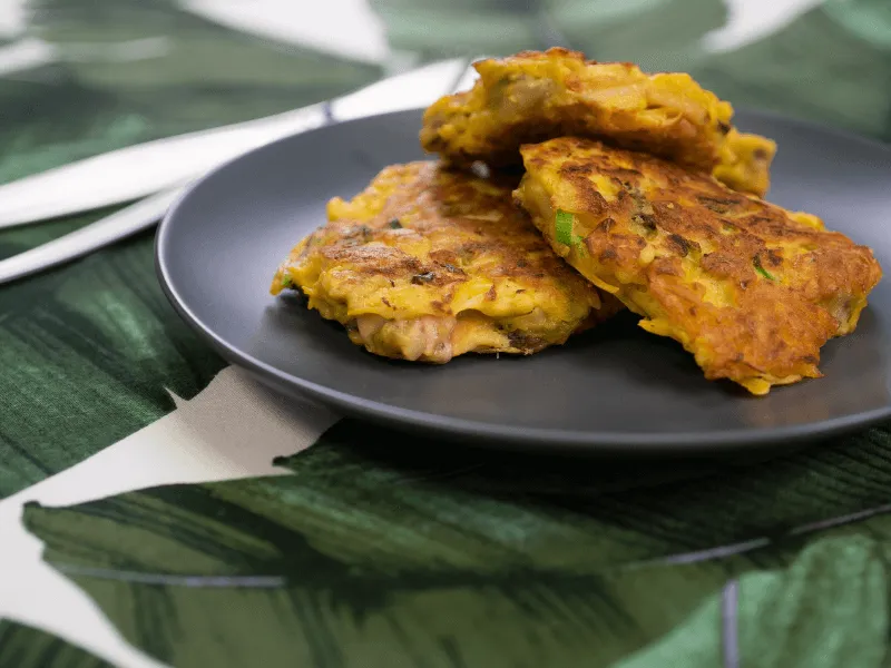 Golden mussel and pumpkin fritters with spring onion, pan‑fried until crisp and served on a dark plate.