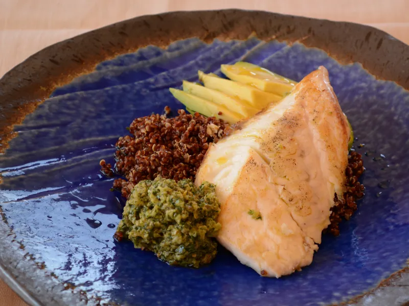 Pan fried fish fillet with red quinoa, salsa verde and sliced avocado on a blue plate.