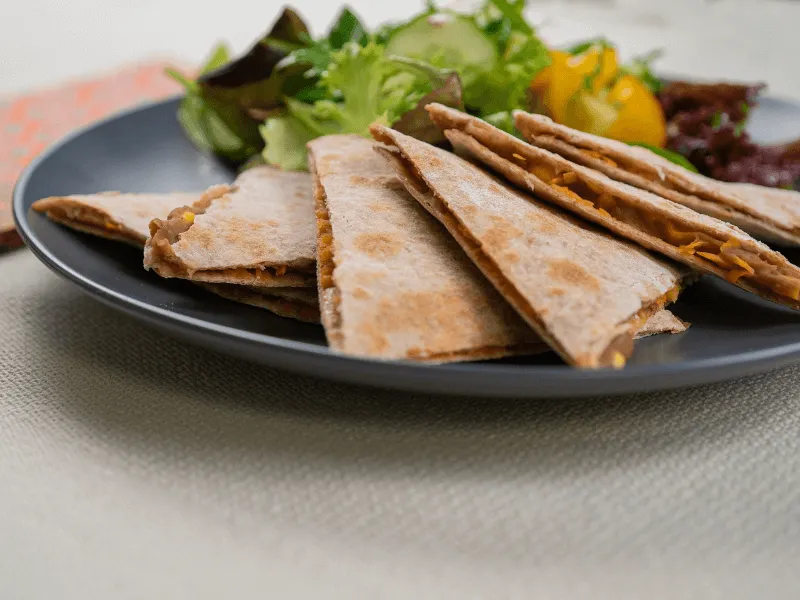 Cheese quesadillas cut into wedges and served with a green salad and salsa on a dark plate.