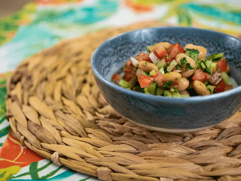 Radish, cucumber, tomato, and white bean salad tossed with fresh herbs and lemon vinaigrette in a blue bowl on a woven placemat.
