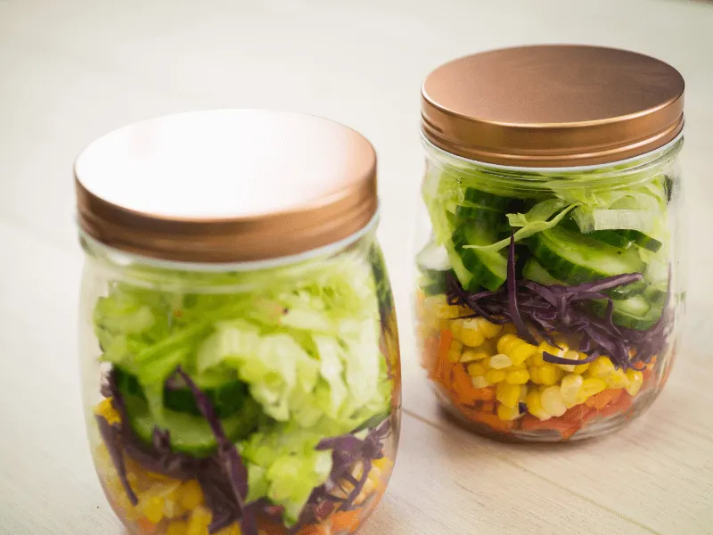 Layered rainbow salad jars filled with capsicum, carrot, corn, red cabbage, cucumber, and lettuce, packed in mason jars for grab‑and‑go lunches.